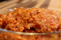 Raw Italian Sausage mixture with red spice coating piled in a glass bowl on a wooden surface.
