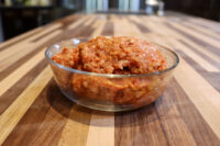 Glass bowl of raw seasoned Italian Sausage mixture on a striped wooden countertop.