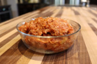 Raw Italian Sausage meat mixed with reddish seasoning in a glass bowl on a wood counter