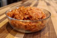 Glass bowl of raw seasoned ground pork for Italian Sausage, mixed with reddish spices on a wooden table
