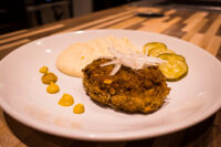 Fried Karbenátky (Czech Burger) patty topped with onion, served with mashed potato, mustard, and pickles.