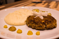 Karbenátky (Czech Burger) patty topped with sliced onion, served with mashed potato, mustard dots, and pickles.
