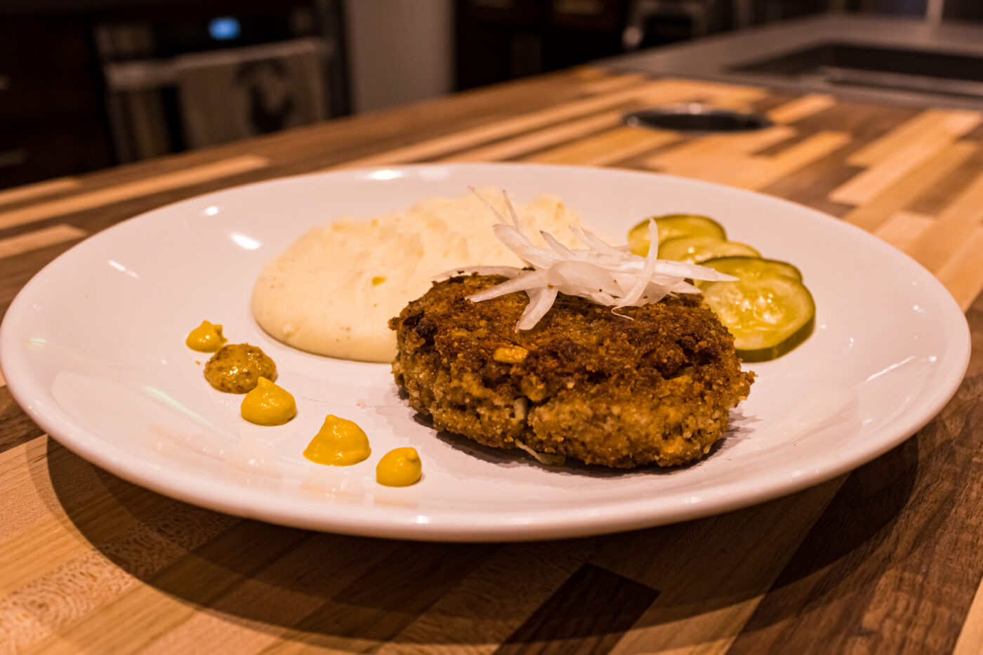 Karbenátky (Czech Burger) patty on a white plate with mashed potato, pickles, and mustard.