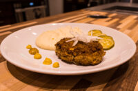 Karbenátky (Czech Burger) patty on a white plate with mashed potato, pickles, and mustard.