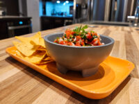 Gray footed bowl of chunky tomato salsa with cilantro, served with tortilla chips on orange tray.