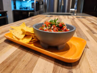 Gray bowl of Salsa with diced tomatoes and cilantro, tortilla chips on an orange tray.