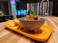 Gray bowl of chunky Salsa topped with herbs, served with tortilla chips on an orange tray.