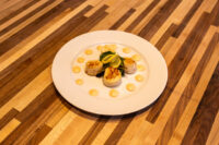 Plate of Scallops with Spicy Sauce, seared scallops on greens with a lemon wedge and yellow sauce dots.