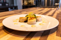 Three seared scallops with lemon twist and yellow sauce dots, plated for Scallops with Spicy Sauce