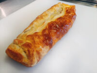 Baked Apple Strudel loaf with braided, golden puff pastry crust on a white cutting board.