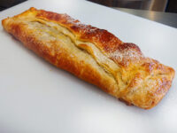 Golden baked Apple Strudel dusted with powdered sugar on a white cutting board.