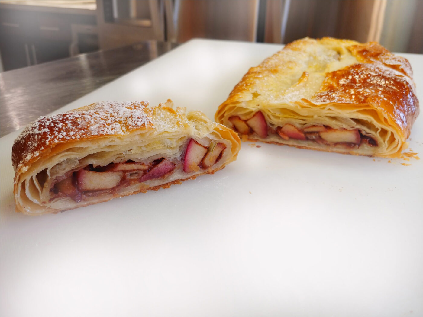 Apple Strudel cut in half, showing fruit filling inside golden puff pastry, dusted with powdered sugar.