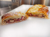 Apple Strudel cut in half, showing fruit filling inside golden puff pastry, dusted with powdered sugar.