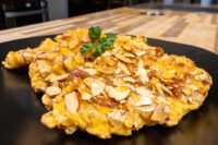 Almond Chicken Schnitzel cutlet crusted in sliced almonds, plated with parsley on a black plate.