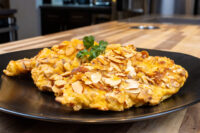Two almond-crusted Almond Chicken Schnitzel cutlets on a black plate with parsley garnish on wood counter