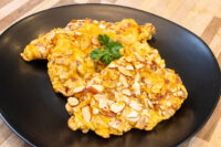 Almond Chicken Schnitzel cutlet with sliced almond crust on a black plate, garnished with parsley.