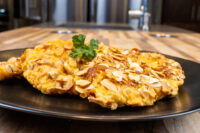 Golden Almond Chicken Schnitzel topped with sliced almonds, garnished with parsley on a black plate.
