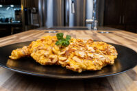 Two almond-crusted Almond Chicken Schnitzel cutlets on a black plate with a parsley garnish.