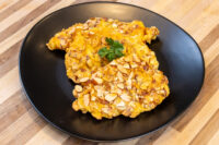 Almond Chicken Schnitzel coated in sliced almonds, garnished with parsley, on a black plate.