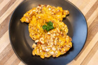 Two almond-crusted Almond Chicken Schnitzel cutlets on a black plate with a parsley garnish.