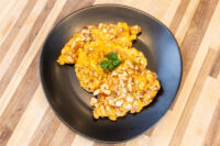 Almond Chicken Schnitzel pieces on a black plate, coated in sliced almonds and garnished with parsley.