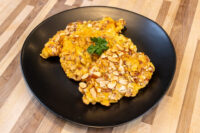 Almond Chicken Schnitzel with a sliced almond crust and parsley garnish on a black plate.