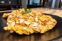 Almond Chicken Schnitzel cutlet coated in golden sliced almonds, garnished with parsley on a black plate.