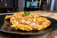 Two almond-crusted Almond Chicken Schnitzel cutlets on a black plate with a parsley sprig.