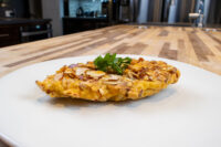 Almond Chicken Schnitzel cutlet coated in sliced almonds, garnished with parsley on a white plate.