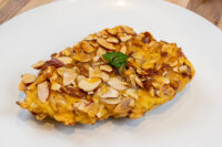 Golden Almond Chicken Schnitzel crusted with sliced almonds, garnished with parsley on a white plate.