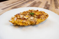 Golden Almond Chicken Schnitzel coated in sliced almonds, garnished with herb, on a white plate.
