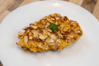 Almond Chicken Schnitzel coated in sliced almonds, garnished with parsley on a white plate.