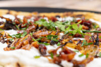 Close-up of Lokše Flat Bread with Bryndza Cheese Substitute and Bacon, showing cheese, onions, bacon, and herbs.