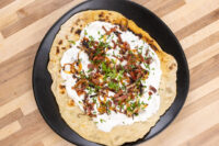 Lokše Flat Bread with Bryndza Cheese Substitute and Bacon topped with white sauce, bacon, onion bits, and chives.