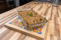 Baked Mushroom Kuba (Houbovy Kuba) in a glass dish, topped with a sprig of herb, on a painted wooden board.