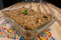 Glass dish of baked Mushroom Kuba (Houbovy Kuba) with barley and mushrooms, garnished with parsley, on a wooden counter.