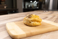 A single golden-baked Pagáče (Pagache) with Cracklings topped with seeds, on a wooden board.
