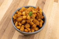Bowl of golden-brown Pork Cracklings (Škvarky) with crispy edges, garnished with a sprig of herb.