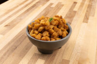 Bowl of golden-brown diced Pork Cracklings (Škvarky), garnished with a green herb leaf, on a wooden table.