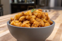 Gray bowl piled with golden-brown Pork Cracklings (Škvarky), topped with a small green herb sprig.