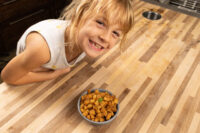 A girl smiles beside a bowl of golden-brown Pork Cracklings (Škvarky) on a wooden counter.