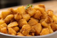 Bowl piled with golden-brown Pork Cracklings (Škvarky), garnished with a small green herb leaf.