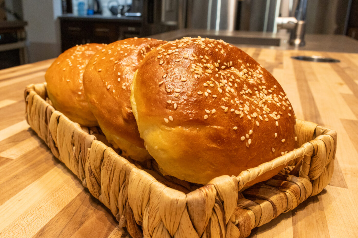 Burger Buns Three sesame-topped Burger Buns arranged in a woven basket on a wooden counter