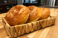 Burger Buns Three sesame-topped Burger Buns arranged in a woven basket on a wood counter.