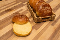 Burger Buns Sliced Burger Bun in front of whole sesame-topped Burger Buns in a woven basket.