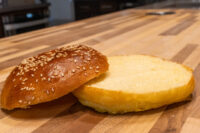 Burger Buns A sesame seed Burger Bun sliced in half, showing its soft interior on a wooden board.