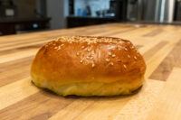 Burger Buns Golden Burger Buns with sesame seeds on top, resting on a wooden countertop.