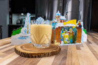 A glass of Czech Egg Liqueur – Czech Eggnog on a wood slice coaster with a Nativity paper cutout behind it