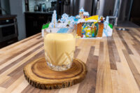 A glass of Czech Egg Liqueur – Czech Eggnog on a wooden coaster with a winter village decoration behind it.