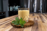 Glass of Czech Egg Liqueur – Czech Eggnog, pale yellow and creamy, on a wood slice with mint.